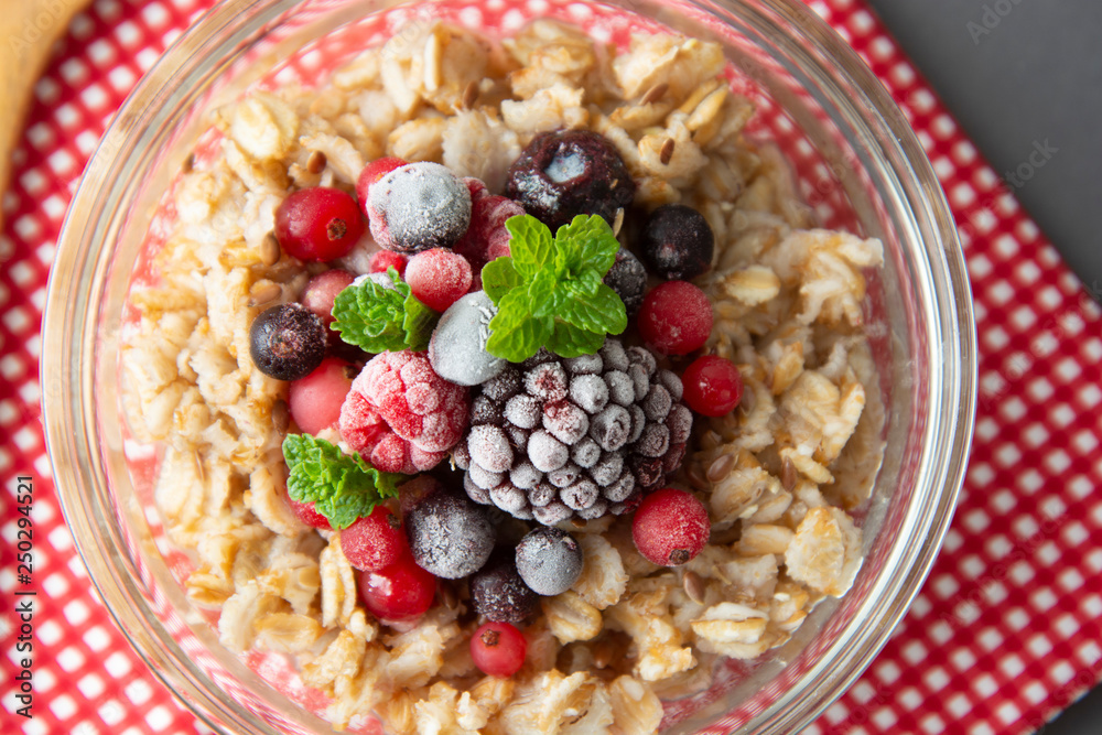 Healthy breakfast in a bowl with oatmeals, frozen berries, fresh strawberries, mint. Oat porridge with fruits. top view.