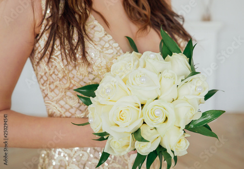 Crop photo of bride in beautiful golden dress with wedding bouquet of white roses in hands, close up