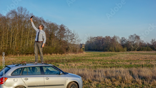 Mann steht auf einem Autodach und versucht Empfang zu finden, um zu telefonieren, weil er eine Autopanne hat