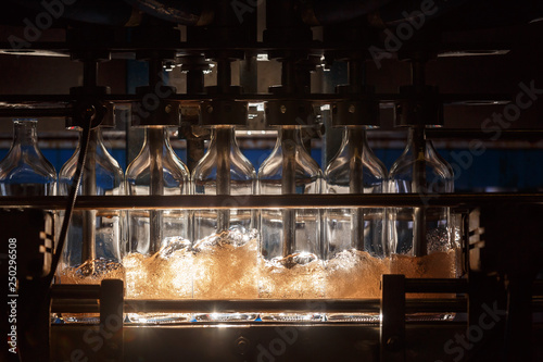 Automatic filling machine pours Liquid into glass bottles. Brewing production. Industrial background.