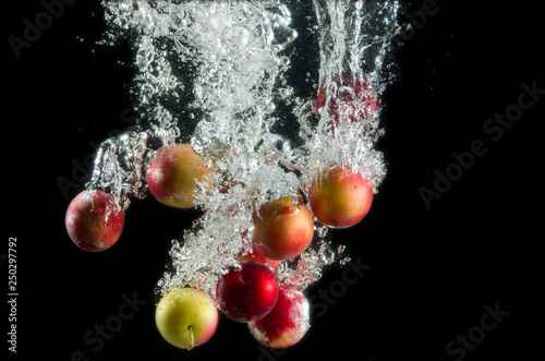 A handful of red and yellow plums in water splash with bubbles on a black background. Photo through the water.