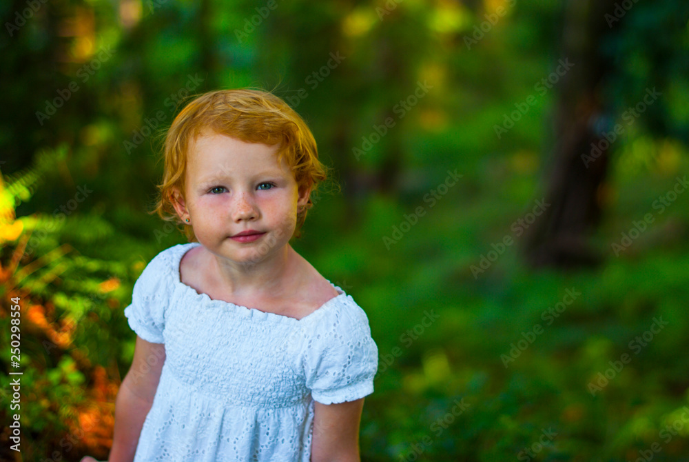Little beautiful red-haired girl in summer in the forest. Baby in white clothes against a forest. Little beautiful red-haired girl in summer in the forest. Baby in white clothes against a forest.