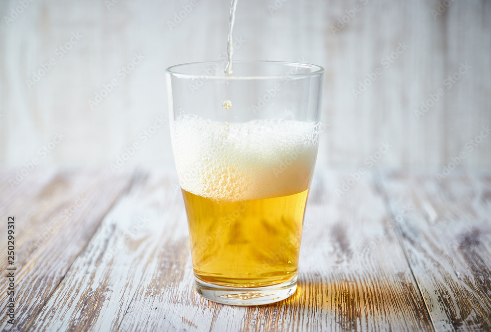 A glass of light beer with foam on a wooden background, close-up. vertical view of the glass. A glass of light beer with foam on a wooden background, close-up. vertical view of the glass.