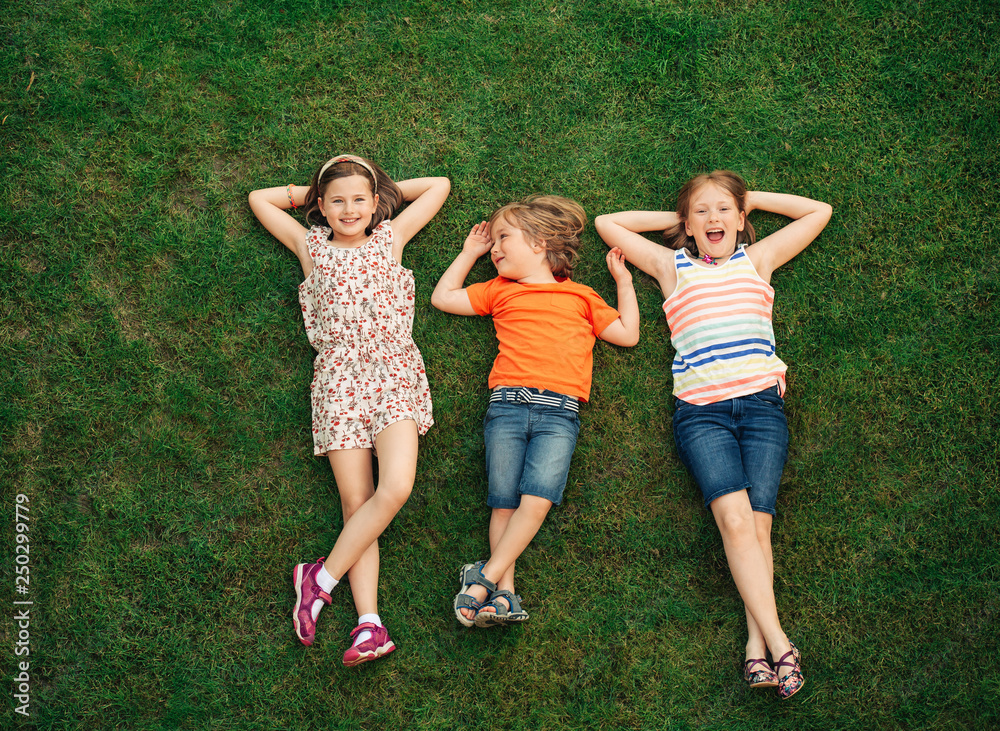 Happy children having fun outdoors. Kids playing in summer park. Little boy and two girls lying on green fresh grass Happy children having fun outdoors. Kids playing in summer park. Little boy and two girls lying on green fresh grass