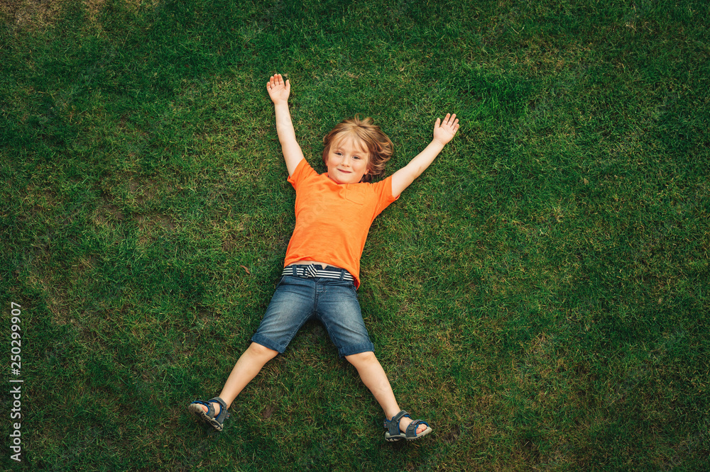 Happy child having fun outdoors. Kid playing in summer park. Little boy lying on green fresh grass, top view Happy child having fun outdoors. Kid playing in summer park. Little boy lying on green fresh grass, top view
