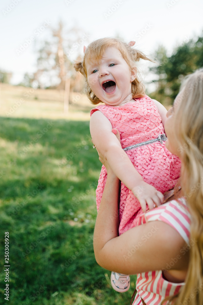 Portrait of a mother holds, throws up and spins the daughter on hands on nature on summer day vacation. Mom and girl playing in the park at the sunset time. Concept of friendly family. Close Up. Portrait of a mother holds, throws up and spins the daughter on hands on nature on summer day vacation. Mom and girl playing in the park at the sunset time. Concept of friendly family. Close Up.