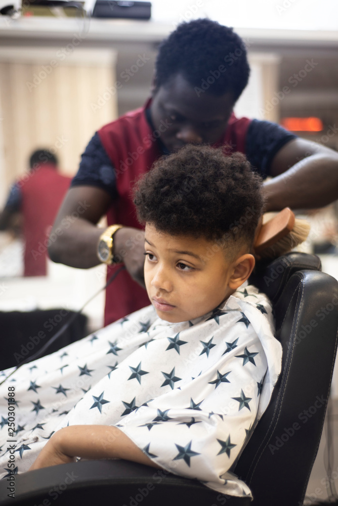 Boy in the african barbershop. Cute mixed boy makes a haircut in the  African salon. Hair style. Haircut by machine for children. School boy hair  style. Stock Photo | Adobe Stock
