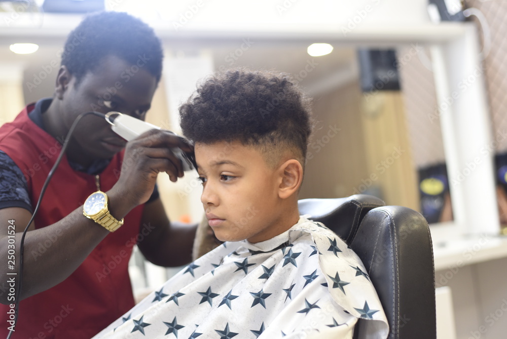 Boy in the african barbershop. Cute mixed boy makes a haircut in the African  salon. Hair style. Haircut by machine for children. School boy hair style.  Stock Photo | Adobe Stock