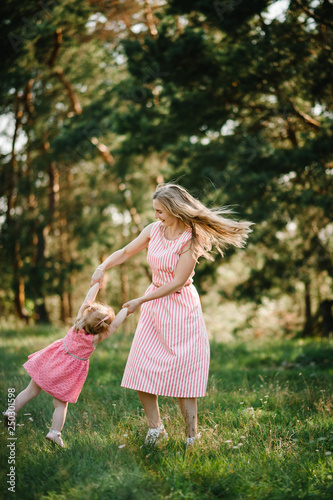 Happy mother spins the daughter on hands on nature on summer day vacation. Mom and girl playing in the park at the sunset time. Concept of friendly family. Close Up.