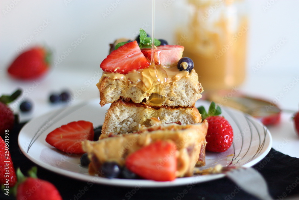 Pouring syrup over french toasts with peanut butter, strawberries and blueberries for breakfast. Pouring syrup over french toasts with peanut butter, strawberries and blueberries for breakfast.