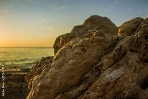 soft focus stone sea shoreline foreground and water surface with horizon line and evening romantic sunset sky background, copy space 