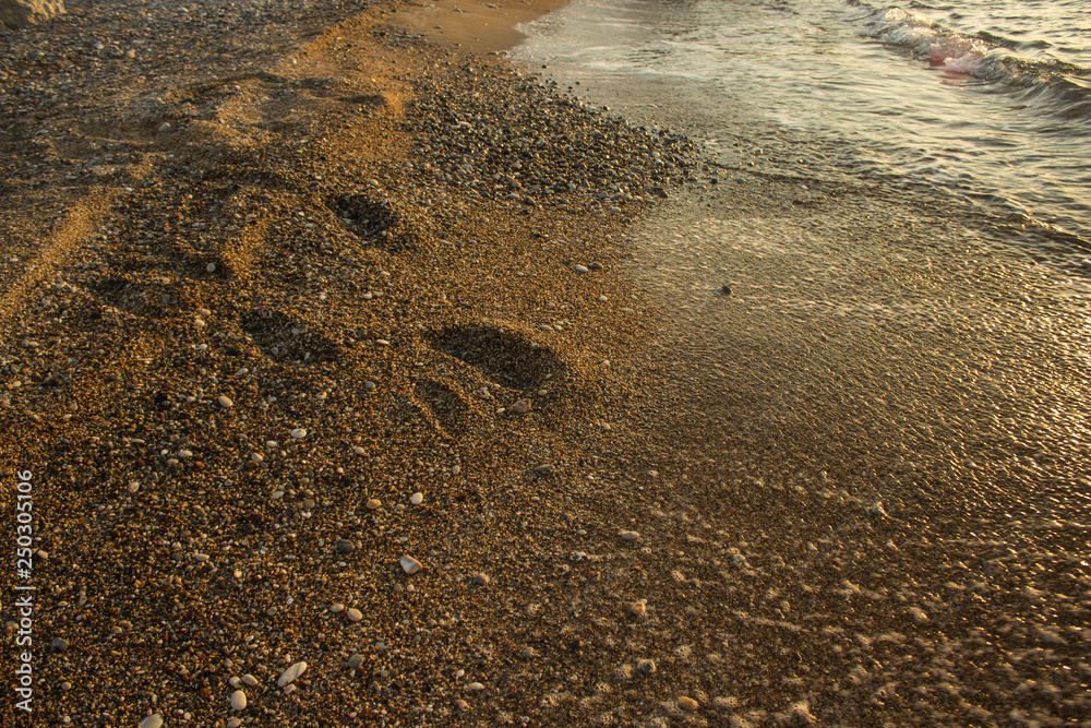 Obraz premium calm idyllic sand beach sea shoreline place near sea water with human foot prints on surface after walking, promenade and vacation concept