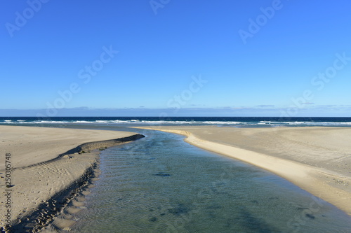 Beach with golden sand  river and blue sea with waves and white foam. Clear sky  sunny day. Galicia  Spain.