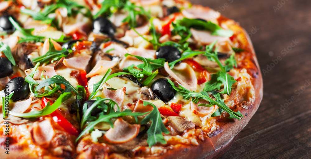 Pizza with Mozzarella cheese, mushrooms, ham, tomato sauce, pepper, olives, Spices and Fresh arugula. Italian pizza on wooden table background Pizza with Mozzarella cheese, mushrooms, ham, tomato sauce, pepper, olives, Spices and Fresh arugula. Italian pizza on wooden table background