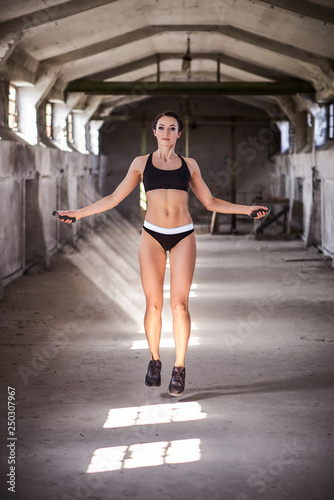 Beautiful woman in sportswear workout with jumping rope in industrial building