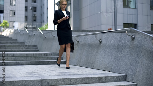 Business lady walking down stairs and texting on smartphone, careerist lifestyle