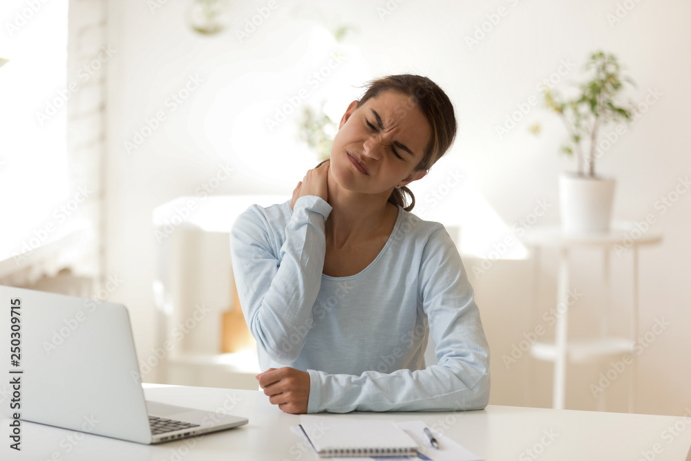 Young female suffers from neck ache at workplace Young female suffers from neck ache at workplace
