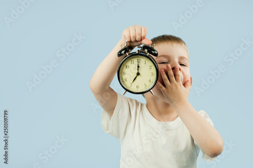 child boy with an alarm clock in his hands early in the morning ziva and does not want to wake up on a photo