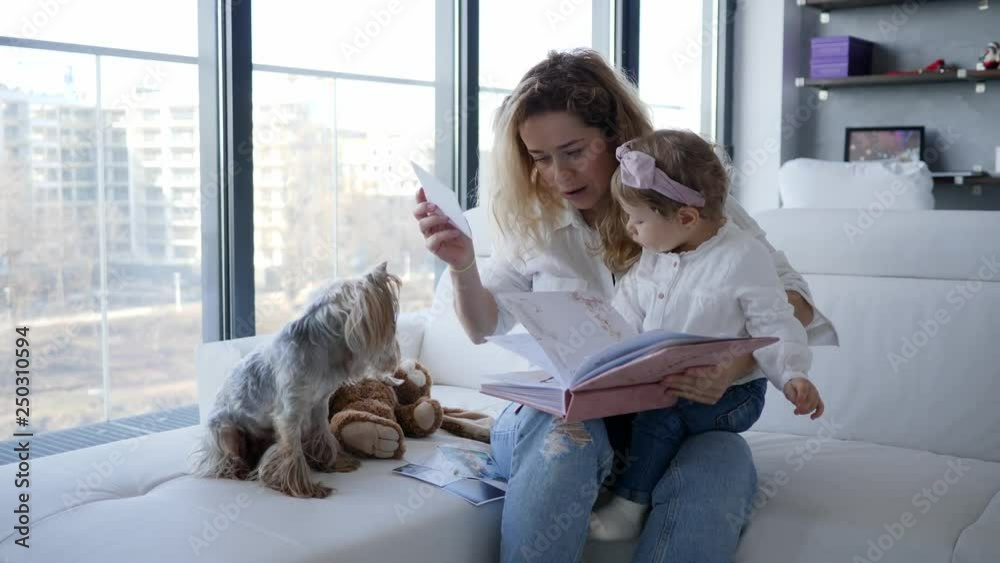 Mother with baby child daughter and pet dog watching family photo album at home Mother with baby child daughter and pet dog watching family photo album at home