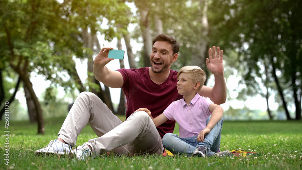 Father and son talking with mother via smartphone, video conference outdoors Father and son talking with mother via smartphone, video conference outdoors