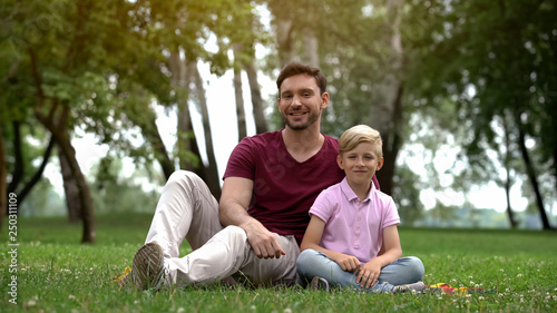 Happy father and son sitting in park, ad of social support for single fathers © motortion