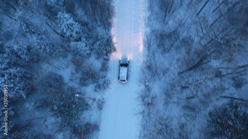 Tracking birdseye drone shot of SUV on snow covered rural road. Evening drive with headlights on, in Northern Ontario, Canada. Winter driving.