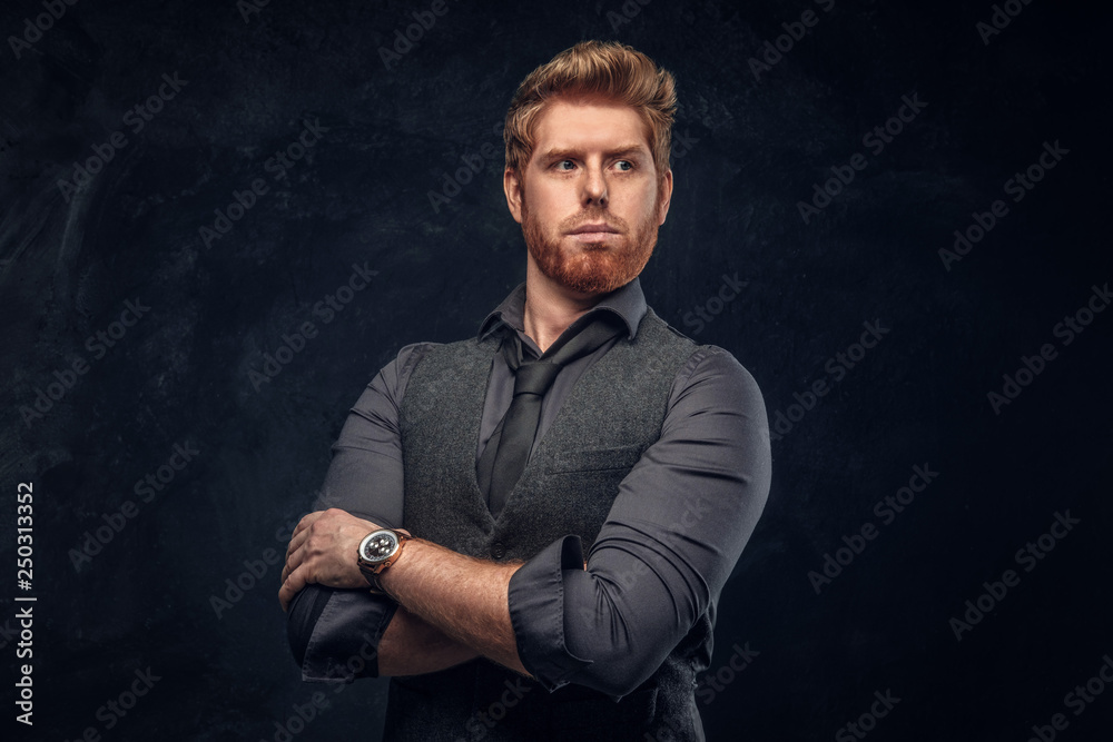 Handsome elegantly dressed redhead man posing with his arms crossed in studio against a dark textured wall