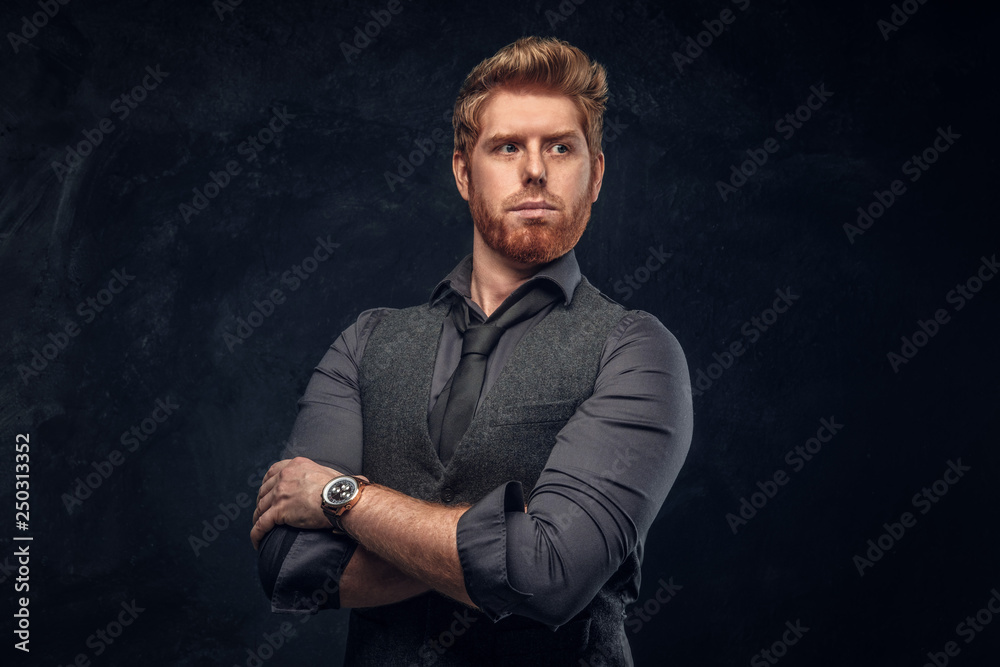 Handsome elegantly dressed redhead man posing with his arms crossed in studio against a dark textured wall Handsome elegantly dressed redhead man posing with his arms crossed in studio against a dark textured wall