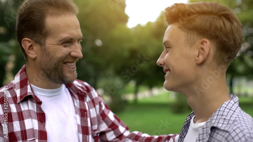 Proud father looking at son, congratulating with entering university, success photo