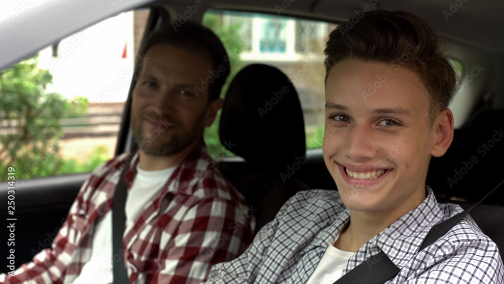 Young driver and his father smiling into camera, teen getting driving license