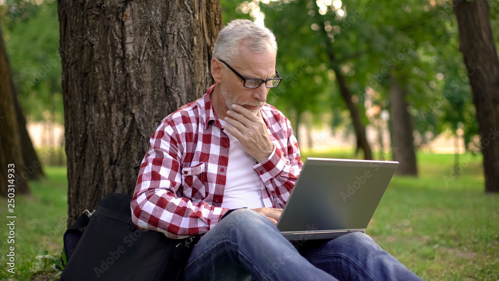 Male pensioner choosing birthday gift online on laptop, man resting in park Male pensioner choosing birthday gift online on laptop, man resting in park