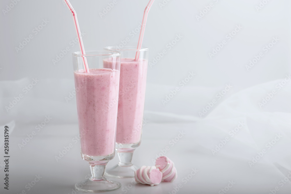 Cocktail has pink color there is in glasses with straws and marshmallows. Strawberry smoothie poured in two glasses, standing on the table. Light key, white and pink colors. Cocktail has pink color there is in glasses with straws and marshmallows. Strawberry smoothie poured in two glasses, standing on the table. Light key, white and pink colors.