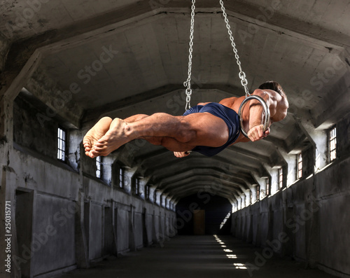 A professional athlete with a beautiful muscular body trains on gymnastic rings in abandoned industrial building