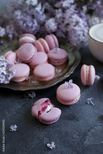 Lavander or blueberry macarons with vanilla ganache on vintage silver plate and dark stone table, decorated with lilac flowers