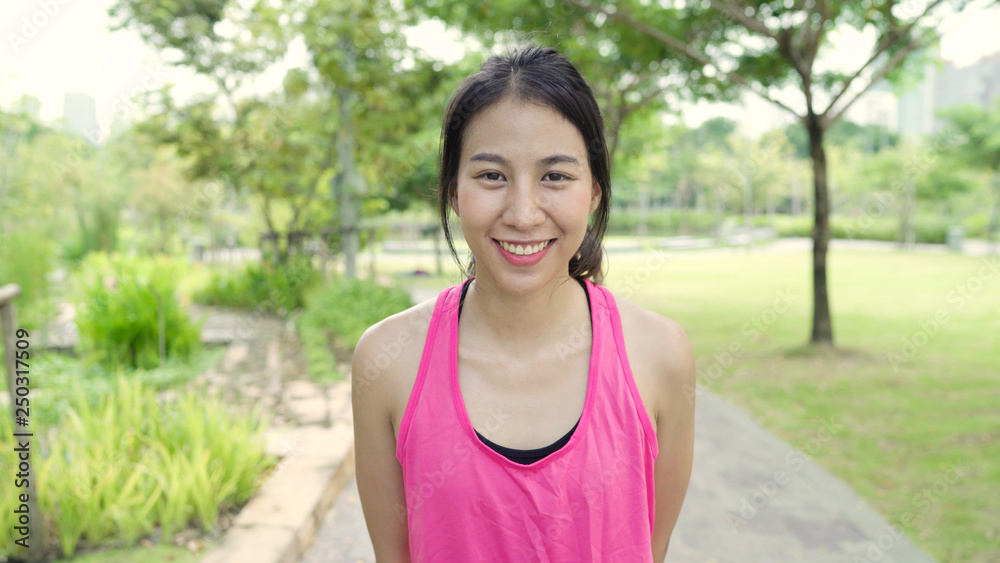 Healthy beautiful young Asian runner woman feeling happy smiling and looking to camera after running on street in urban city park. Lifestyle fit and active women exercise in the city park concept. Healthy beautiful young Asian runner woman feeling happy smiling and looking to camera after running on street in urban city park. Lifestyle fit and active women exercise in the city park concept.