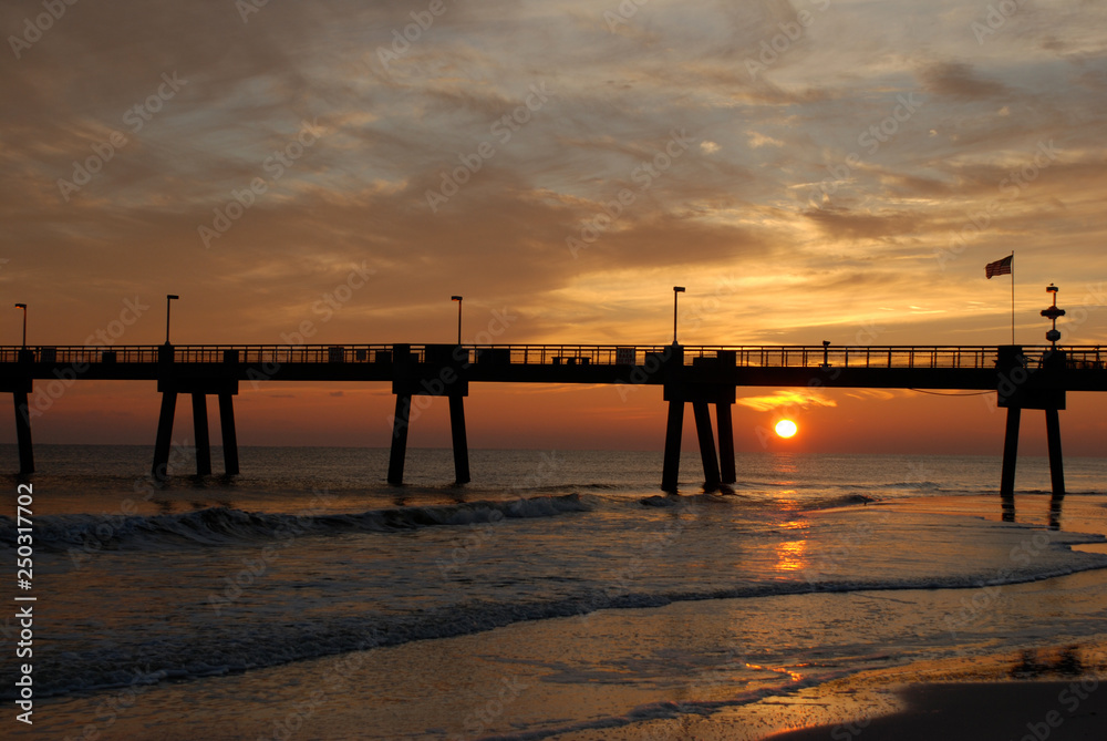 Sun setting under the pier in Destin, Florida, while waves crash onto the beach