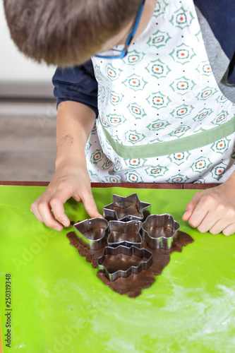 Dłonie chłopca wyciskającego kształty z metalowych foremek z ciasta położonego na zielonej silikonowej stolnicy. Zajęcia kulinarne dla dzieci.