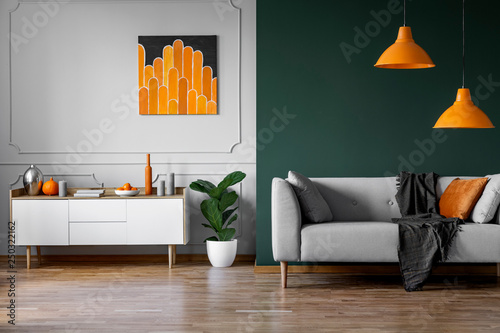 Fototapeta Naklejka Na Ścianę i Meble -  Abstract orange painting on grey wall of stylish living room interior with white wooden furniture and grey couch