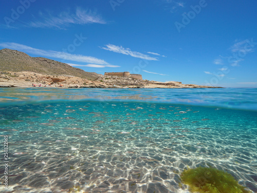 Spain Mediterranean coast with a castle and school of fish (bogue) with sand underwater sea, el Playazo de Rodalquilar, Almeria, Andalusia, split view half over and under water