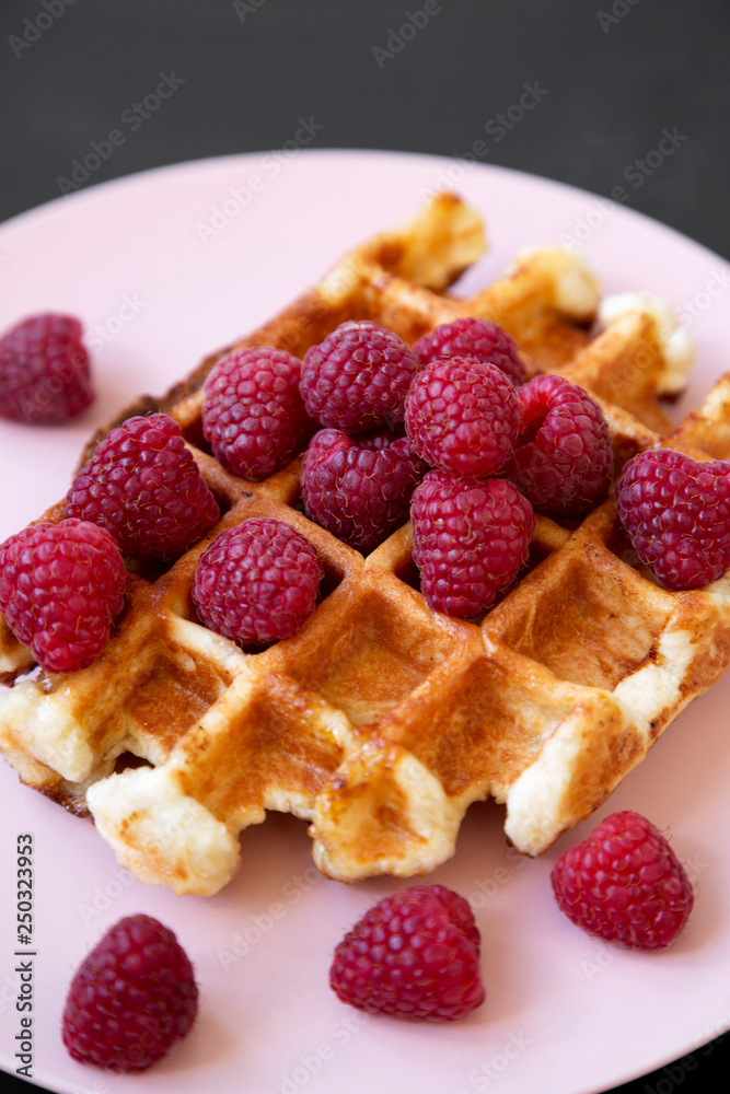 Traditional belgian waffle with raspberries on pink plate over black table, close-up. Traditional belgian waffle with raspberries on pink plate over black table, close-up.
