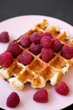 Traditional belgian waffle with raspberries on pink plate over black table, close-up.