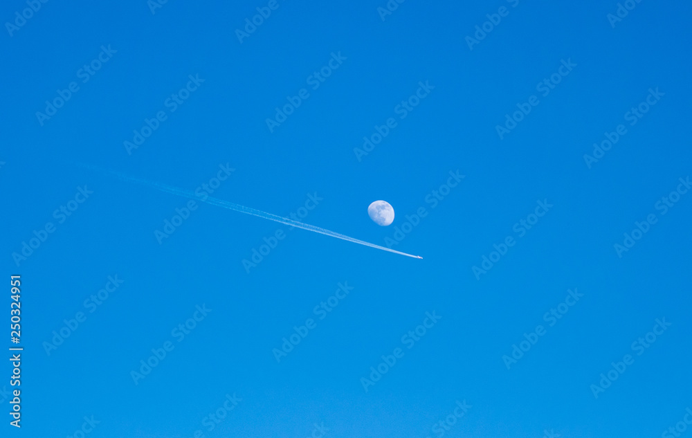 Image of airplane with condensation trails flying next to the detailed moon Image of airplane with condensation trails flying next to the detailed moon