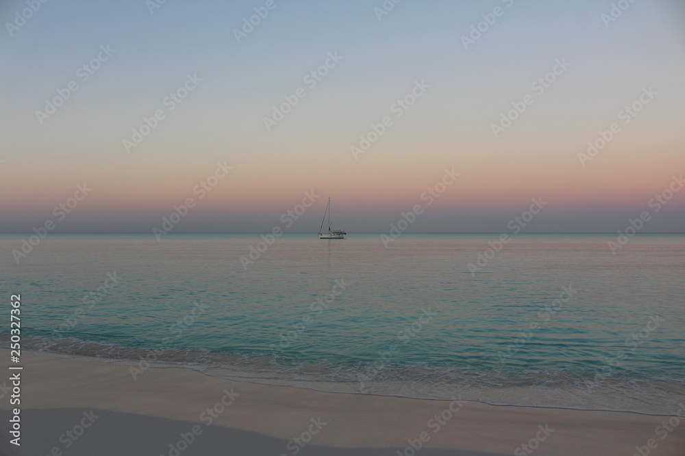 Sunset lights on the sea with a sailboat in the background, Long Island, Bahamas