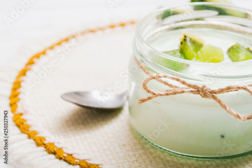 Yogurt with kiwi slices on a wooden white background.