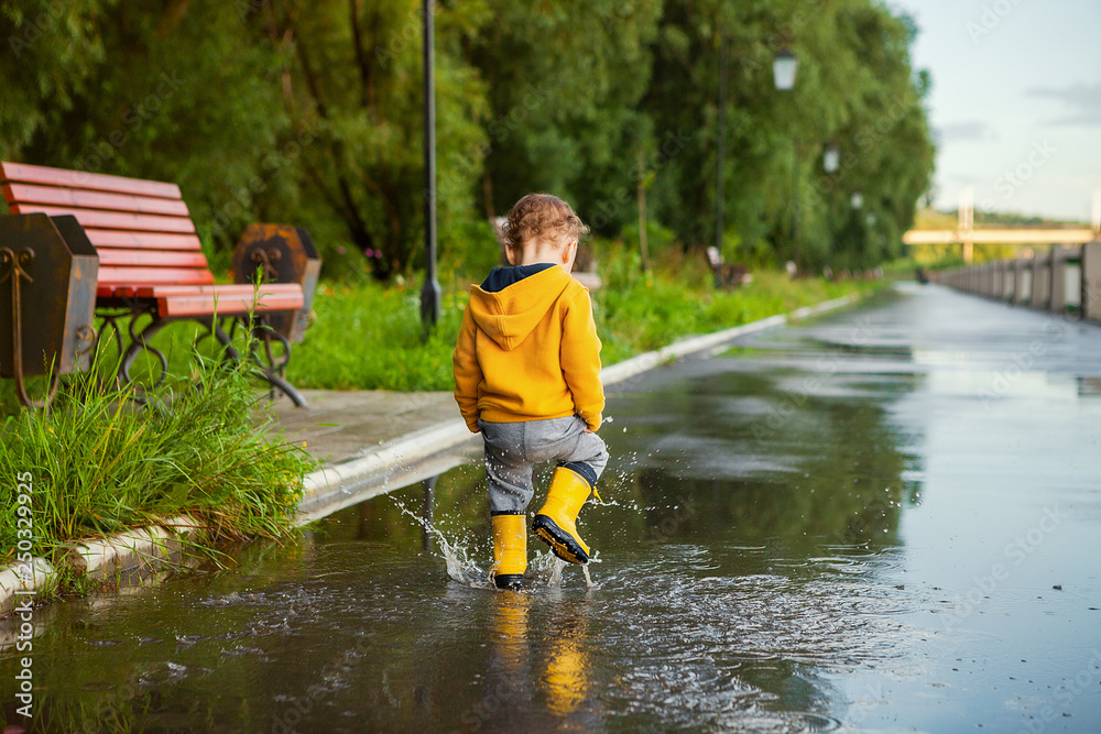 small boy in yellow raincoat playing in puddles small boy in yellow raincoat playing in puddles