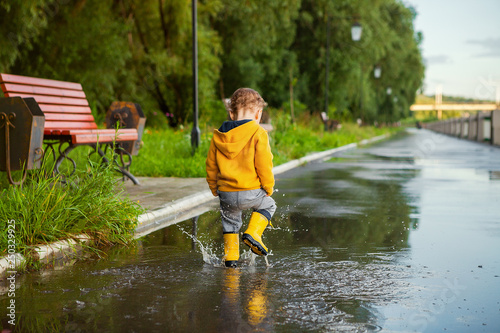 small boy in yellow raincoat playing in puddles