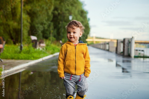Portrait of beautiful smiling kid boy. Happy child against green tree background. Kid playing outdoors. Laughing healthy boy in yellow rain coat
