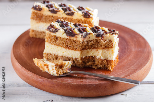 a piece of cake with milk and butter cream cutted with spoon on a wooden kitchen board, white background.. © zgurski1980