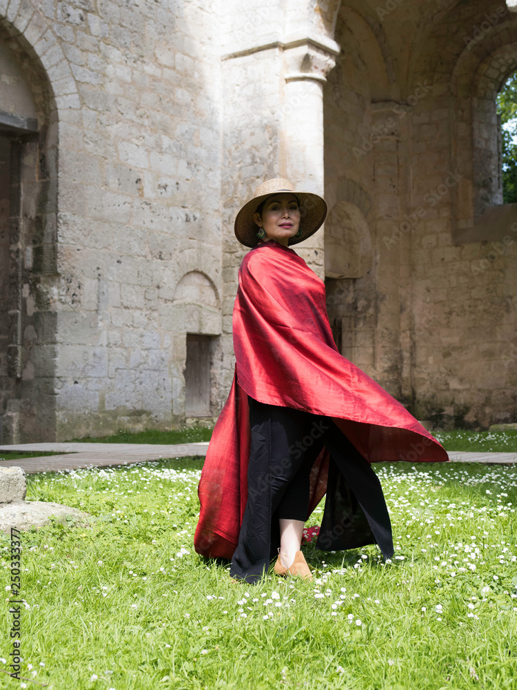 Femme agitant une étoffe de soie rouge dans les ruines d'un monastère moyen-âgeux.