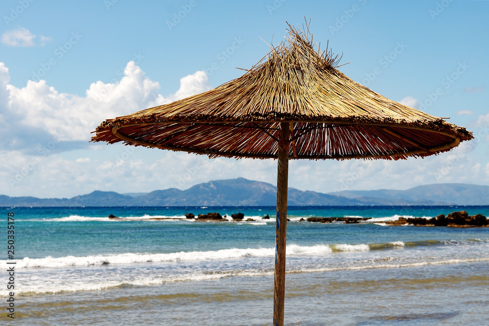 Wicker, beach umbrella on a beautiful, empty beach overlooking the sea and mountains.